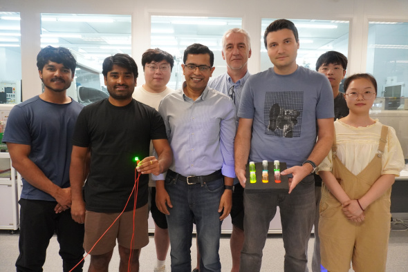 Abhishek K. Srivastava教授（前排中間）、Maksym Prodanov博士（前排右二）和Kumar Mallem（前排左二）與其研究團隊成員合影。Prodanov博士手持的三個瓶子內，載有量子棒材料。Mallem則手持綠色發光QRLED樣本。