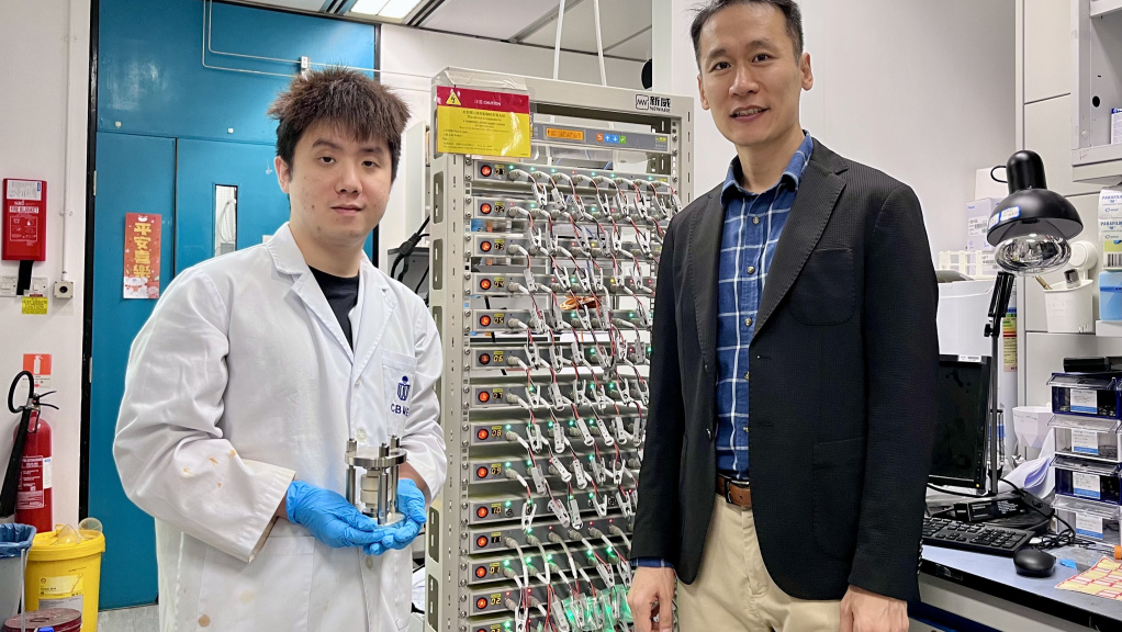 科大化學及生物工程學系副教授兼論文的通訊作者金允燮教授（右）和其博士生兼論文第一作者古穆華（左；手持固態電池模具）站在電池充放電循環儀旁合影。