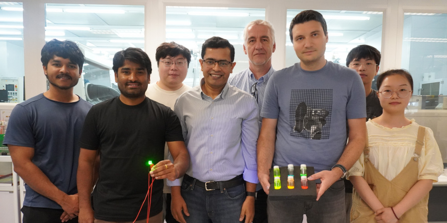 A group photo of Prof. Abhishek K. Srivastava (first row, center), Dr. Maksym Prodanov (first row, second right) and PhD candidate Mr. Kumar Mallem (first row, second left) with members of their research team. In the photo, Dr. Prodanov holds three bottles with quantum rod materials while Mr. Mallem holds a green emitting QRLED sample. 