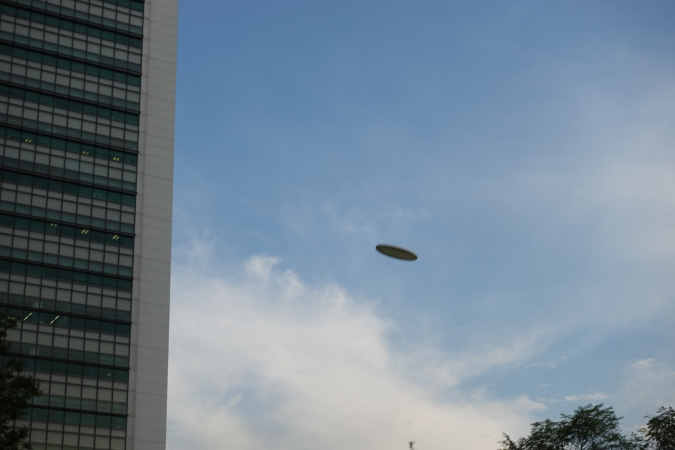 It shows a frisbee flying in the sky of NUS Utown town green.