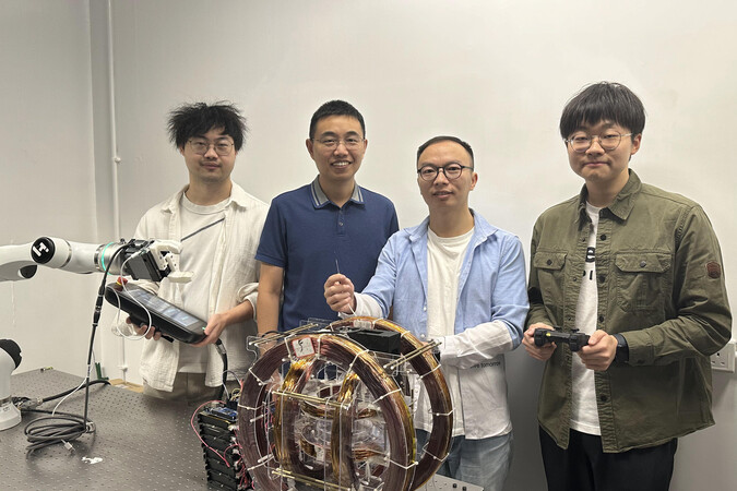 The research team, led by Prof. Shen Yajing (second left) from the Department of Electronic and Computer Engineering, has designed an optical fiber-based submillimeter continuum robot for interventional treatment in narrow cavities, which looks like a small tube as the one held by Dr. Zhang Tieshan (second right) in the photo. The devices held by Dr. Yang Xiong (first left) and Zhao Haoxiang (first right) serve as controllers for the robot arm and the magnetic field, respectively.