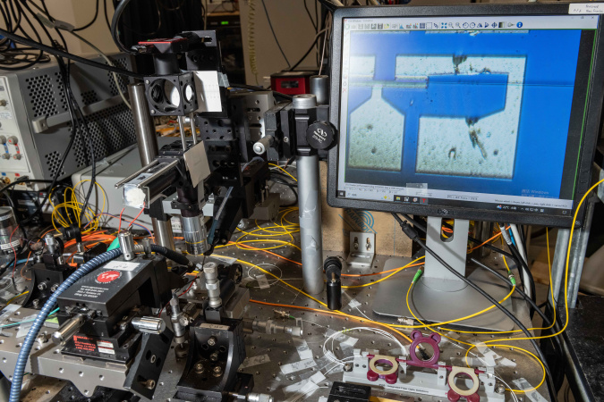 团队利用显微镜观察芯片，右边屏幕展示了锗离子注入的硅波导光电二极管探测器。