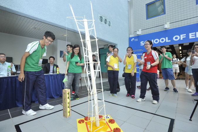 The paper tower needs to carry six tennis balls to pass the loading test.