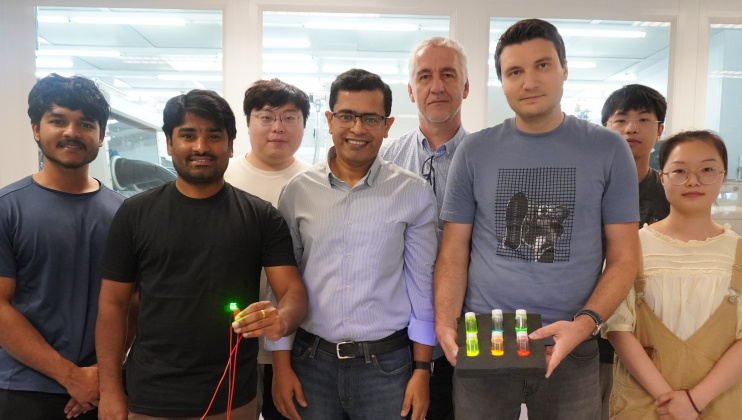 Abhishek K. Srivastava教授（前排中间）丶Maksym Prodanov博士（前排右二）和Kumar Mallem（前排左二）与其研究团队成员合影。Prodanov博士手持的三个瓶子内，载有量子棒材料。Mallem则手持绿色发光QRLED样本。