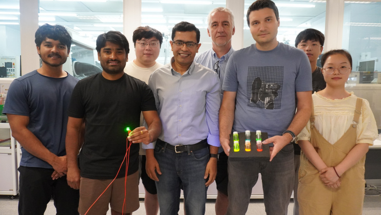 A group photo of Prof. Abhishek K. Srivastava (first row, center), Dr. Maksym Prodanov (first row, second right) and PhD candidate Mr. Kumar Mallem (first row, second left) with members of their research team. In the photo, Dr. Prodanov holds three bottles with quantum rod materials while Mr. Mallem holds a green emitting QRLED sample. 